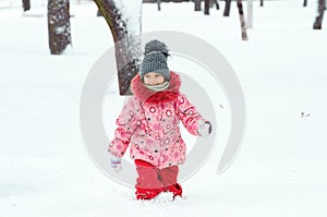Portrait of a beautiful toddler girl playing outdoors with snow. Happy little child enjoying a winter day in the park or