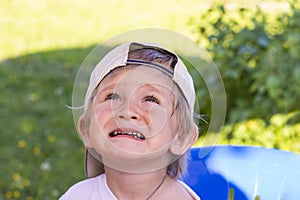 Portrait of a beautiful two year old baby in a baseball cap. A boy with blond hair is carefully looking up somewhere.