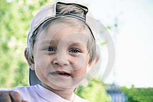 Portrait of a beautiful two year old baby in a baseball cap. A boy with blond hair is looking at the camera and smiling.