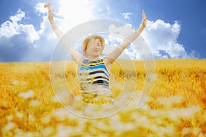 Portrait of beautiful very happy blonde woman with arms outstretched in a wheat field in summer sun`s rays