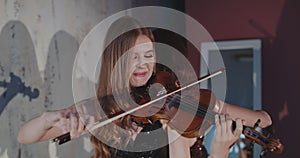 Portrait of beautiful violinist plays music in duet at camera indoor