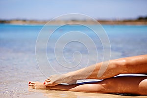 Portrait of a beautiful woman in bikini, hat and sunglasses lying on exotic tropic sea beach. Legs close up