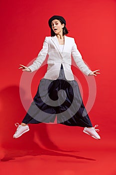Portrait of beautiful woman in black beret and white jacket posing in a jump isolated over red studio background