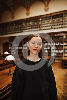 Portrait of a beautiful woman in black clothes in a public library and looking at the camera with a serious face