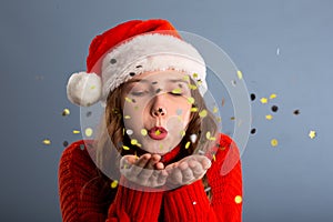 Portrait of beautiful woman blowing confetti in the air, party new years eve celebration on gray background
