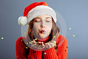 Portrait of beautiful woman blowing confetti in the air, party new years eve celebration on gray background