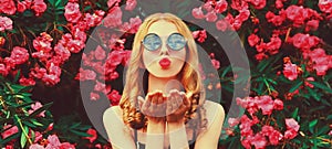 Portrait of beautiful woman blowing her lips with red lipstick sending sweet air kiss on pink roses flowers background