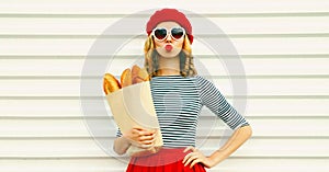 Portrait of beautiful woman blowing her red lips sending sweet air kiss holding grocery shopping paper bag with long white bread