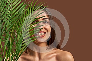 Portrait of a beautiful woman on a brown background holding a branch from a palm tree and smiling. Beauty concept