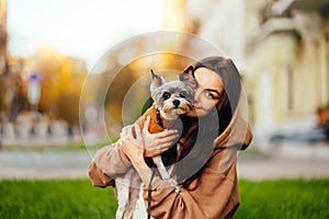 Portrait of a beautiful woman in casual clothes sitting on a city lawn and posing at camera with a cute dog breed biewer terrier