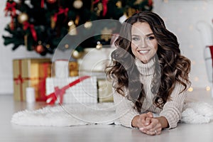 Portrait of a beautiful woman with curls at the Christmas tree with gifts of new year lights garland photo