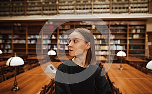 Portrait of a beautiful woman in dark clothes standing in the public library of the university campus and looking away