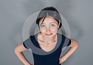 Portrait of  beautiful woman with dark hair wearing  dark t-shirt. Looking at  camera. Gray background. Top view. Hands on hips