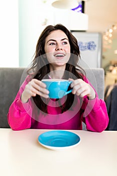 Portrait of beautiful woman drinking a cup of tea in cafeteria. Happy woman in a cafe drinking coffee and looking at camera.