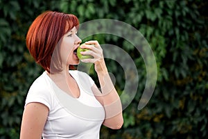 Portrait of beautiful woman eating big green apple outdoors. Freshness, eco-friendly lifestyle and healthy food concept