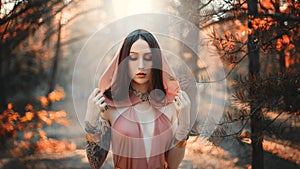 Portrait of beautiful woman fantasy elf in autumn forest. Dark trees background, fog park. Girl princess in orange peach