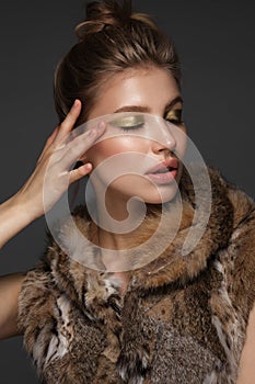 Portrait of a beautiful woman in a furcoat with creative gold makeup in a fashion style. Beauty face.