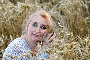 Portrait of beautiful woman with green eyes sitting in golden wheat field and hold bunch of wheat ears. Liberty, love concept