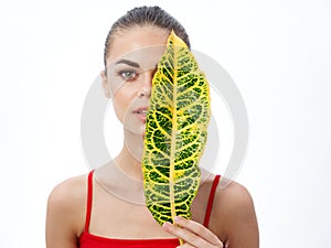 portrait of a beautiful woman with a green leaf in front of her eyes on a light background natural look clear skin