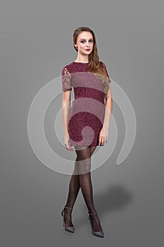 Portrait of beautiful woman on grey background. slim young woman in burgundy bodycon dress posing in studio.