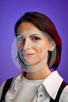 Portrait of beautiful woman in her 30s with short hair, looking at camera against purple studio background in neon light