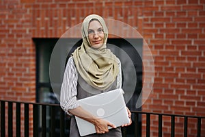 Beautiful woman in hijab standing on city street. Muslim businesswoman with laptop in hands. Iran, Afganistan female photo