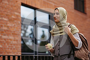 Beautiful woman in hijab standing on city street. Muslim studnet eating apple, going to school. Iran, Afganistan female photo