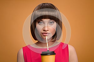 Portrait of beautiful woman holding cup of coffee takeaway in her hand. Yellow background