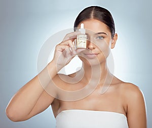 Portrait of beautiful woman holding face serum over eye while posing with copyspace. Young caucasian model isolated