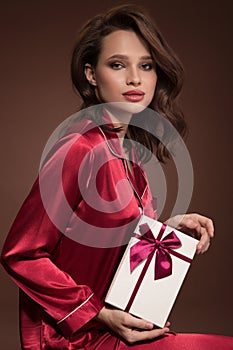 Portrait of beautiful woman holding gift box in her hand. Brown background