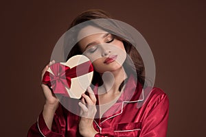 Portrait of beautiful woman holding gift box in her hand. Brown background