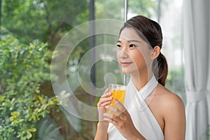 Portrait of a beautiful woman holding a glass of orange juice looking at you sitting at home