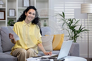 Portrait of beautiful woman at home, businesswoman smiling and looking at camera sitting on sofa in living room at home