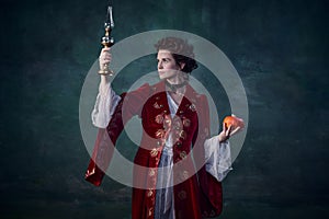 Portrait of beautiful woman in image of medieval vampire holding candle and pumpkin isolated over dark green background photo