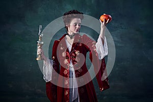 Portrait of beautiful woman in image of medieval vampire holding candle and pumpkin  over dark green background