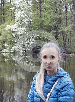 Portrait of a beautiful woman by the lake next to a blooming bird cherry