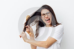 portrait of a beautiful woman in a light T-shirt trying to comb her long tangled hair with a wooden comb and screaming