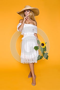 Portrait of a beautiful woman with long blond hair, wearing a white dress, holding sunflowers.