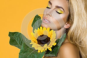 Portrait of a beautiful woman with long blond hair, wearing a white dress, holding sunflowers.