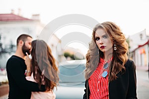 Portrait of beautiful woman with make up looking at camera sadly against unfocused kissing couple.