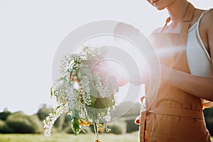 Portrait of beautiful woman making wreath of flowers dandelions on flowering field. Summer lifestyle, nature lover and freedom