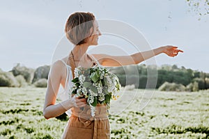 Portrait of beautiful woman making wreath of flowers dandelions on flowering field. Summer lifestyle, nature lover and freedom