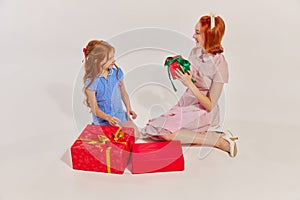 Portrait of beautiful woman, mother giving present to her daughter  over grey studio background. Winter holidays