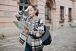 Portrait beautiful woman with paper map on urban street. Young worried female traveler using map lost in the city