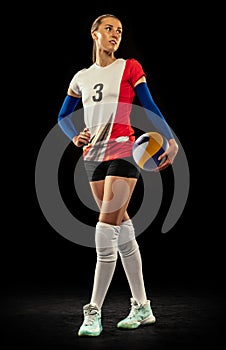 Portrait of beautiful woman, professional volleyball player posing with ball  on dark background. Sport, healthy