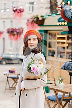 Portrait of a beautiful woman in a red beret and coat with a bouquet of flowers walks down the street