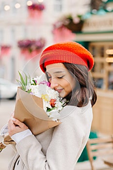 Portrait of a beautiful woman in a red beret and coat with a bouquet of flowers walks down the street