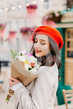 Portrait of a beautiful woman in a red beret and coat with a bouquet of flowers walks down the street