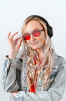 Portrait of a beautiful woman in red glasses and headphones listening to music, enjoying freedom, cool blonde on a white