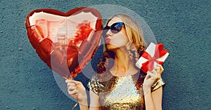 Portrait of beautiful woman with red heart shaped balloons and gift box on dark background